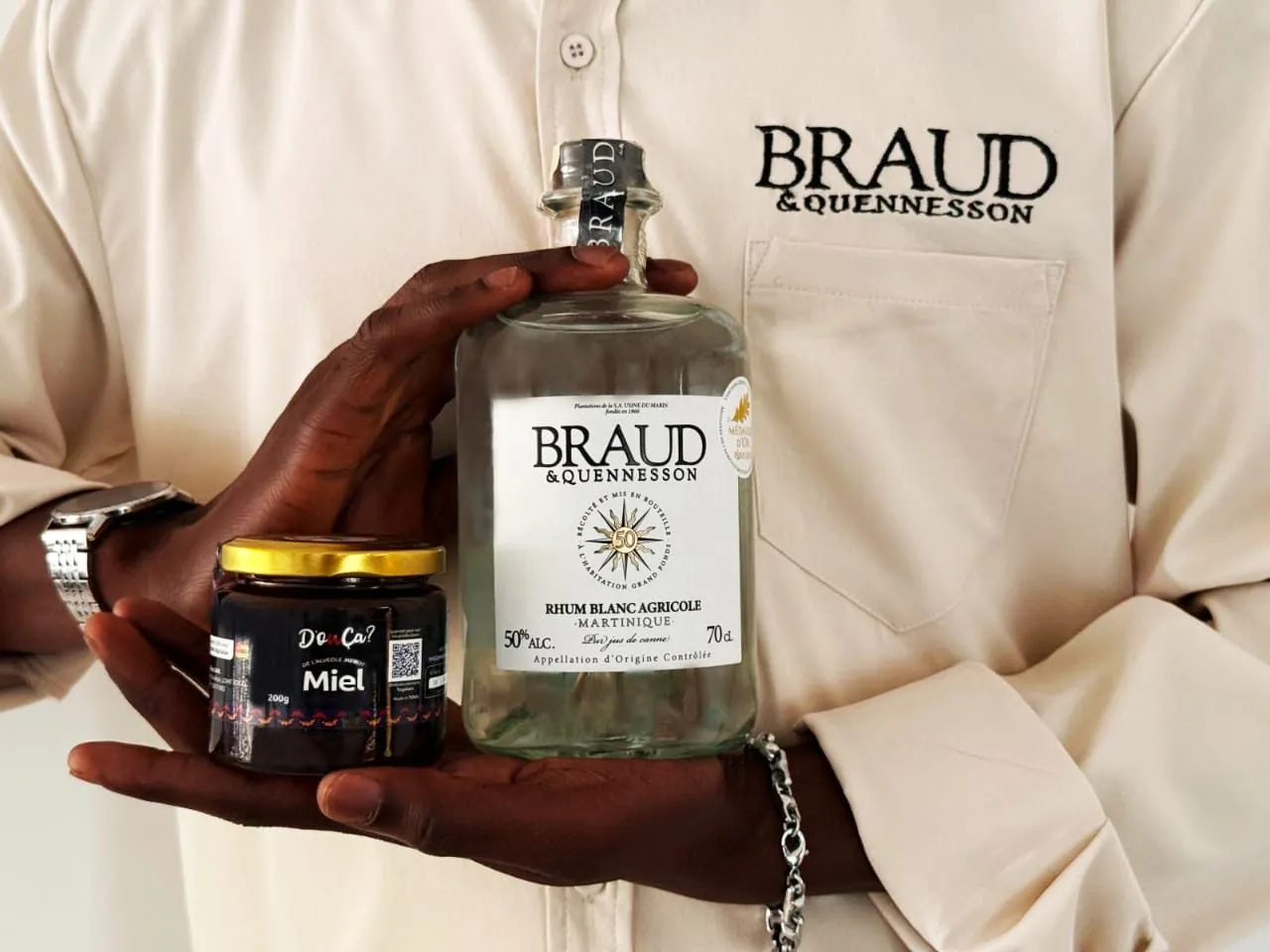 Un rhum blanc agricole Braud & Quennesson de Martinique tenu à côté d'un pot de miel D'oùça?
