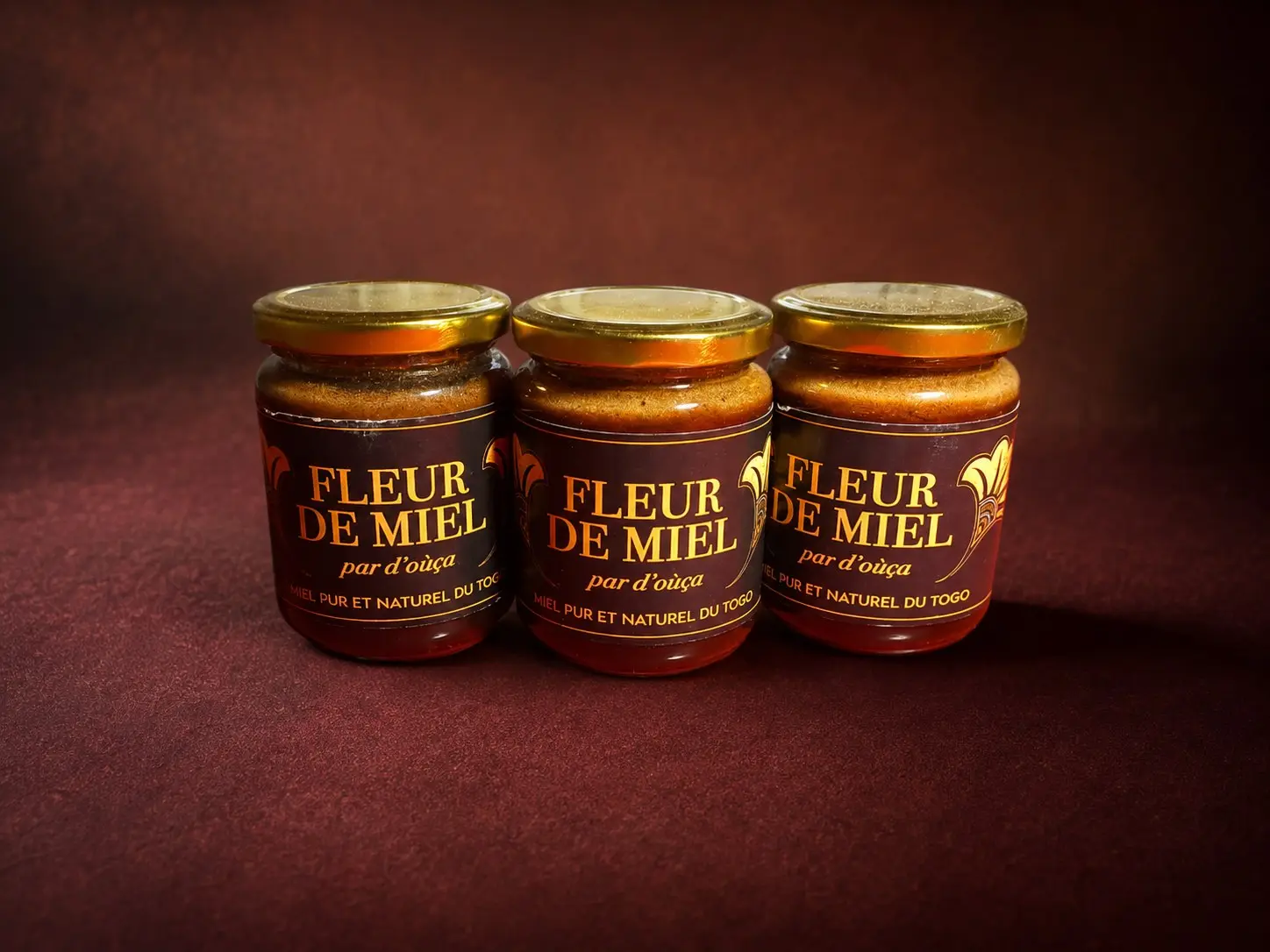 Three jars of D'oùça? Fleur de miel, gold labels on a deep red background